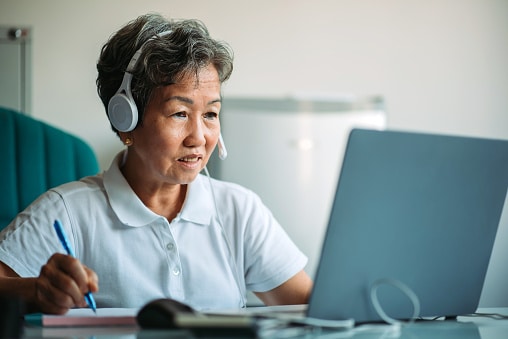 mature woman writing on note pad with laptop on desk