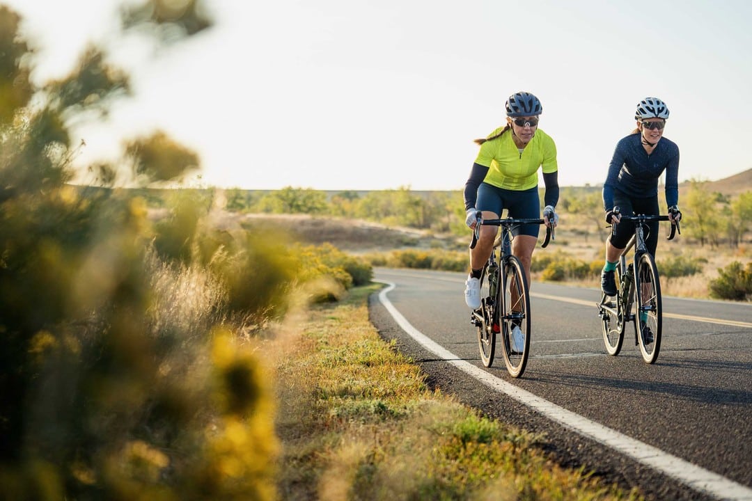 two people riding bikes on an open road with trees around