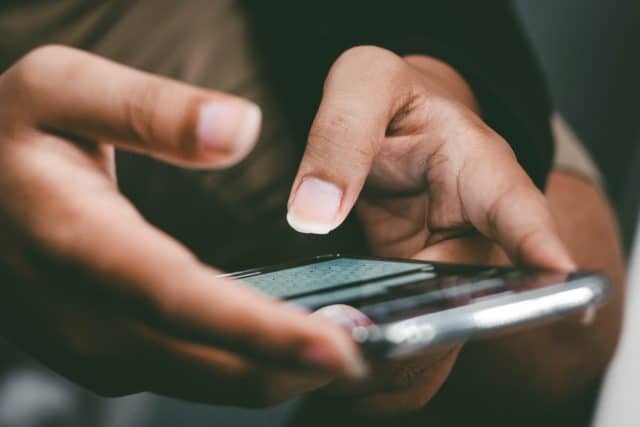 hand holding cell phone. Thumbs out to text or chat. 