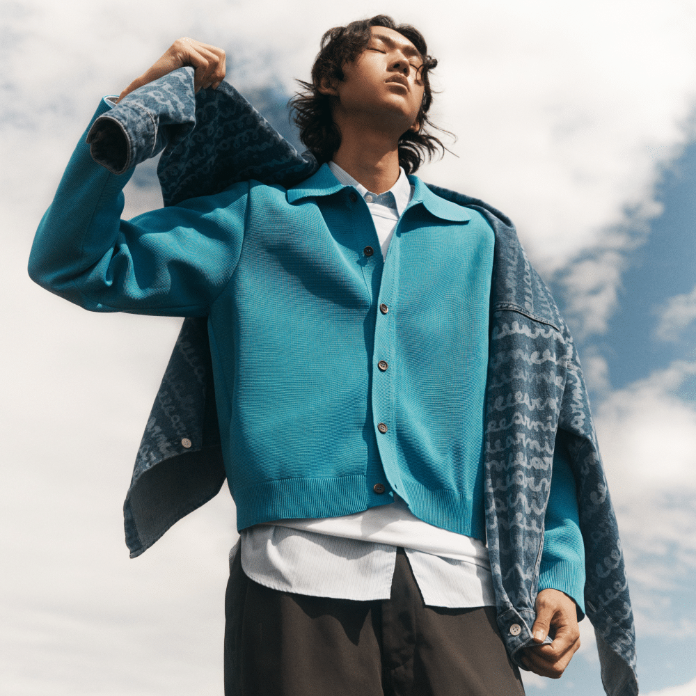 man in blue-green sweater with cardigan over shoulders, blue sky