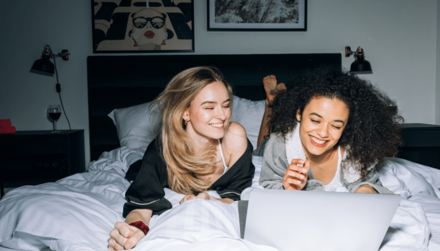 two women online shopping while laying on a bed